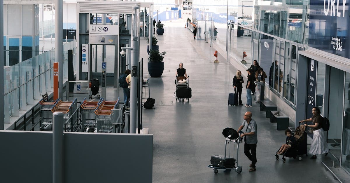 Travellers navigate a wide airport terminal corridor pulling suitcases and luggage trolleys