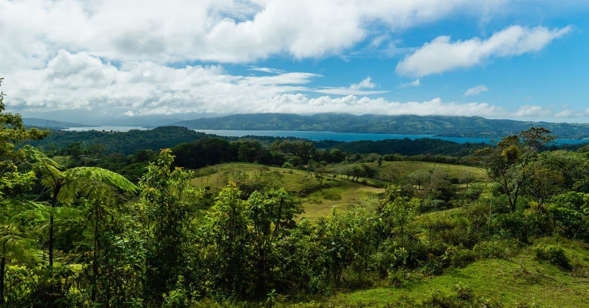Green hills and forest overlook a blue lake beneath a partly cloudy sky in Costa Rica.
