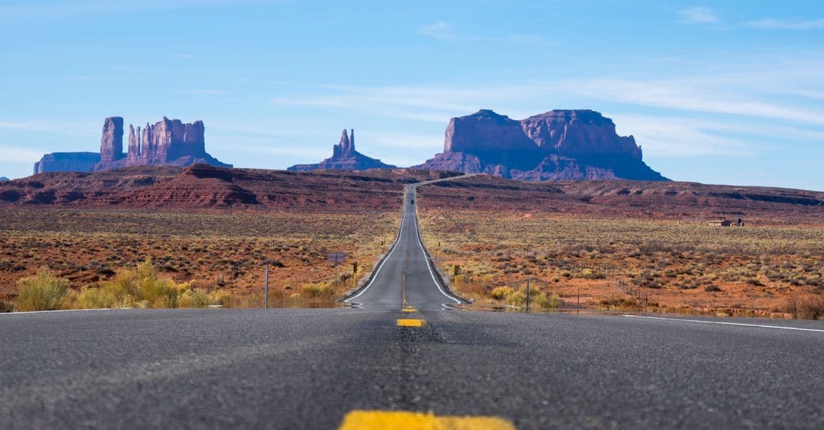 Una strada dritta attraversa la Monument Valley verso grandi rocce rosse, sotto un cielo azzurro.