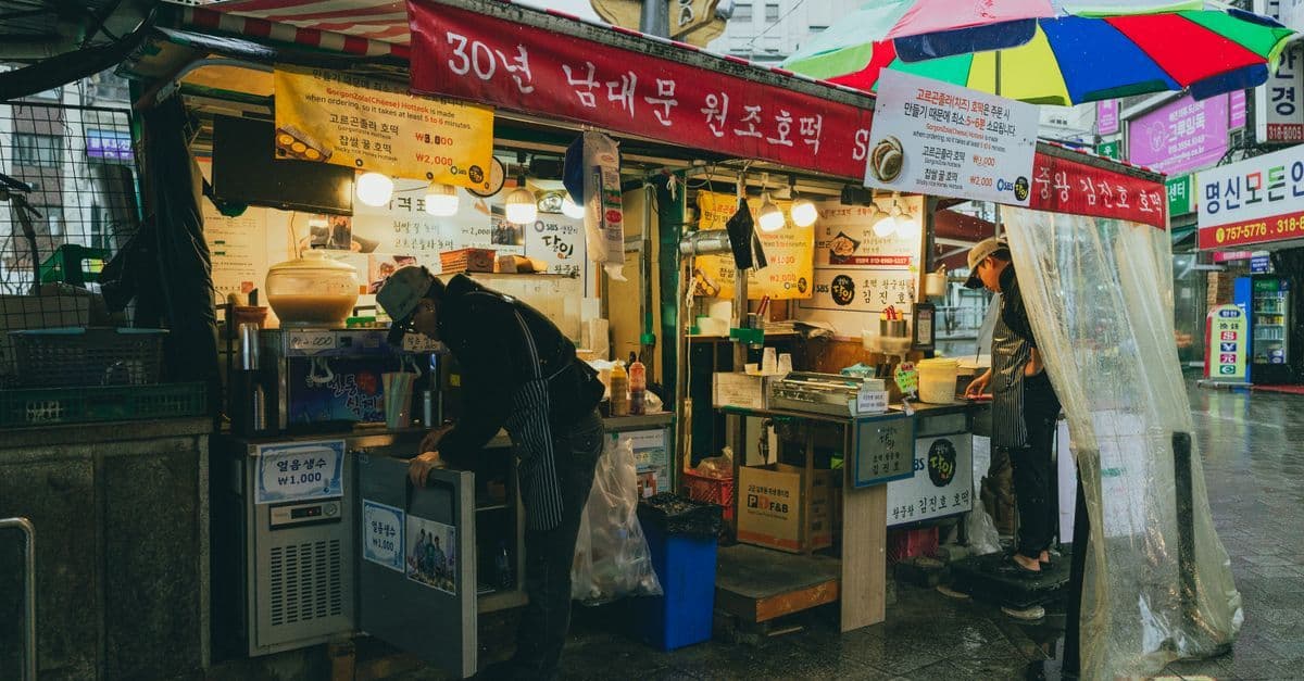ソウルの雨の市場で賑わう韓国屋台の定番メニューと2026年最新グルメトレンド