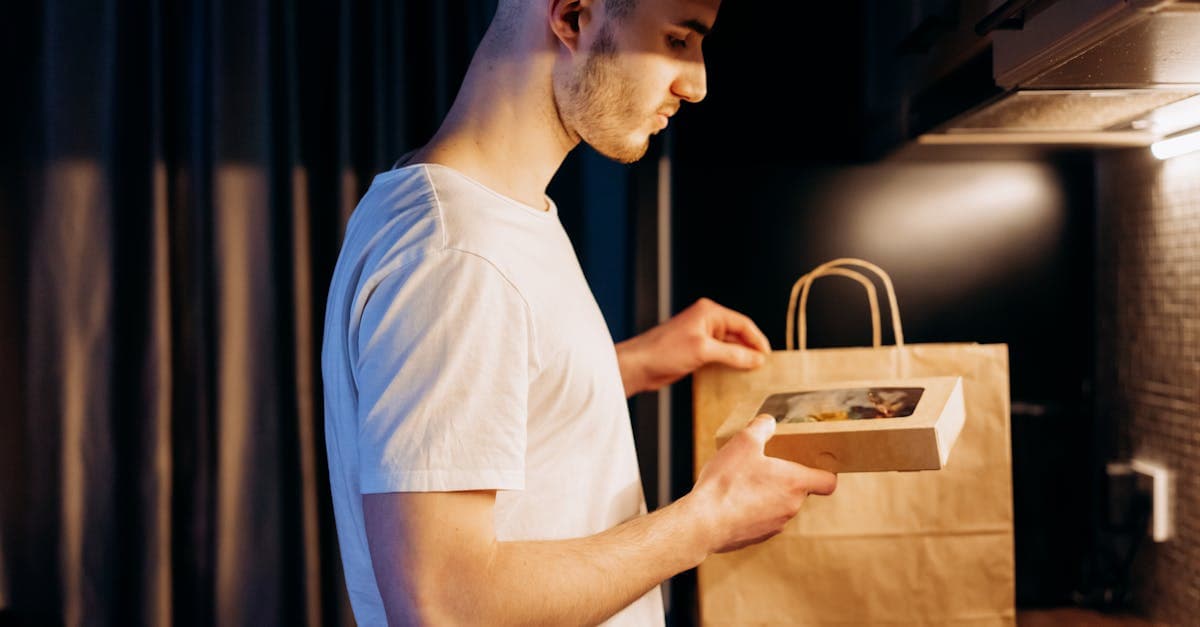 Mann öffnet eine Lebensmittellieferung aus einer Papiertüte in gemütlicher Küche nach einer Food Meal Delivery Bestellung.