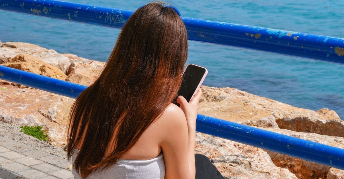 UK traveller using a smartphone by the sea to stay connected with a travel eSIM in Ibiza.