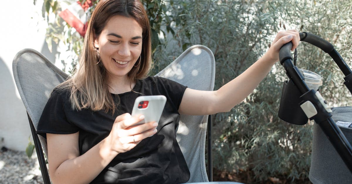 Mother smiles while checking her smartphone beside a stroller, staying connected on holiday abroad