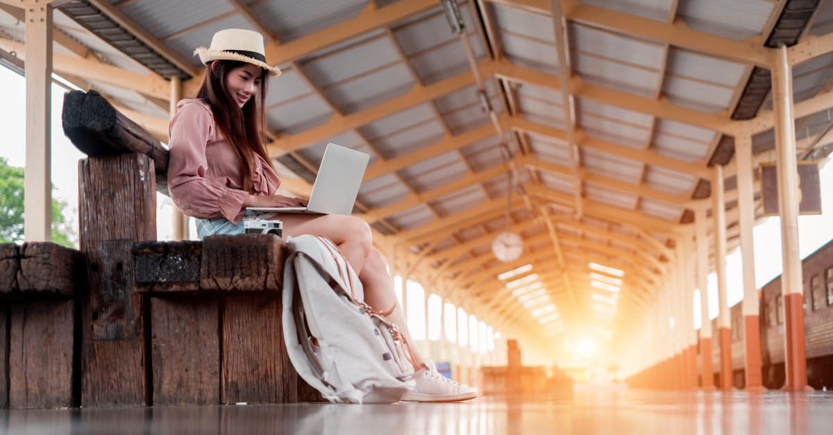 Woman with laptop at sunlit train station, showing traveling alone tips for staying digitally connected