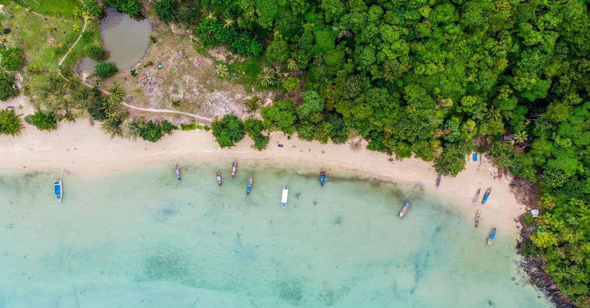 Luftaufnahme eines tropischen Strandes in Krabi mit Booten und dichtem Regenwald während des Südwestmonsuns.