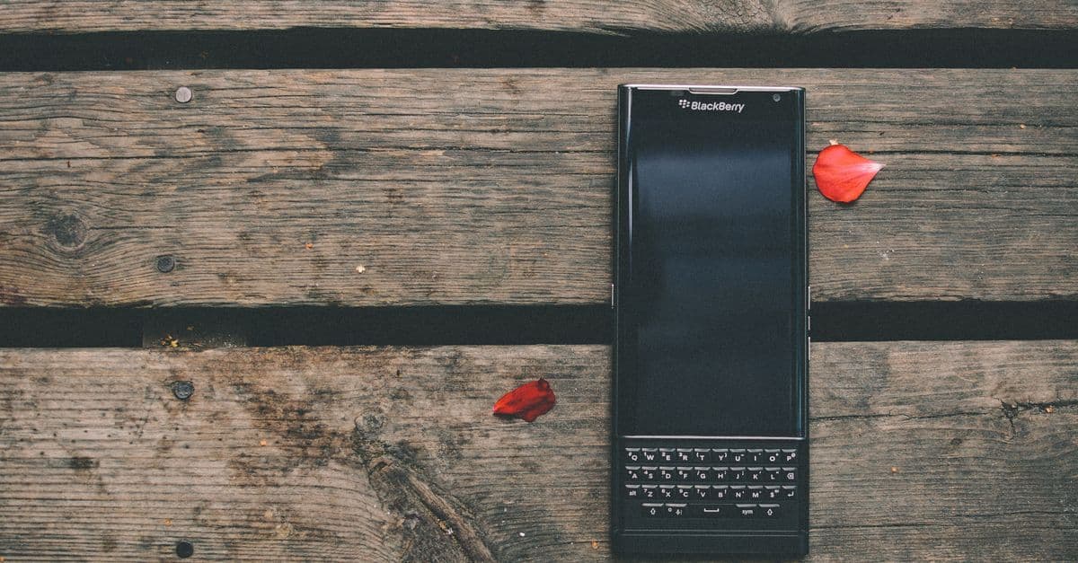 Vintage blackberry phone on a rustic wooden table surrounded by scattered red flower petals outdoors.