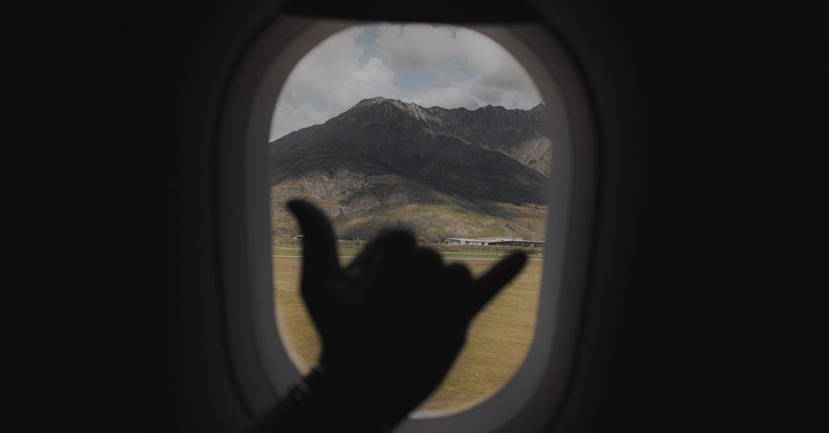 Hand making shaka sign through airplane window overlooking Queenstown mountains and lake below.![image