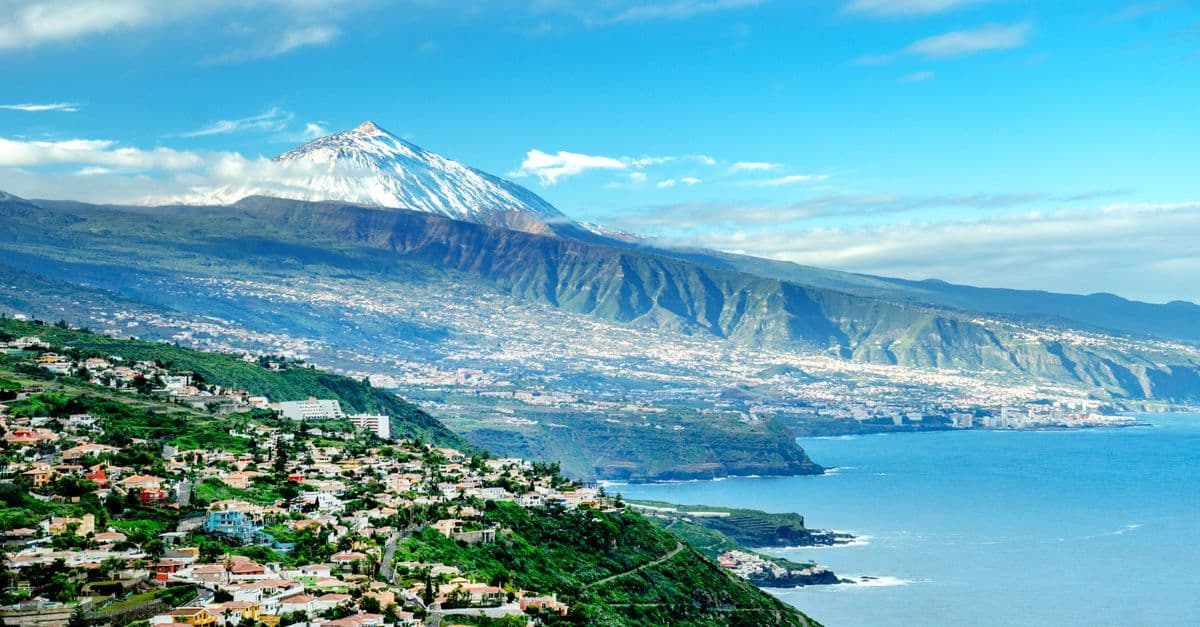 Snow-capped Mount Teide above green hillsides and towns on Tenerife's north coast.