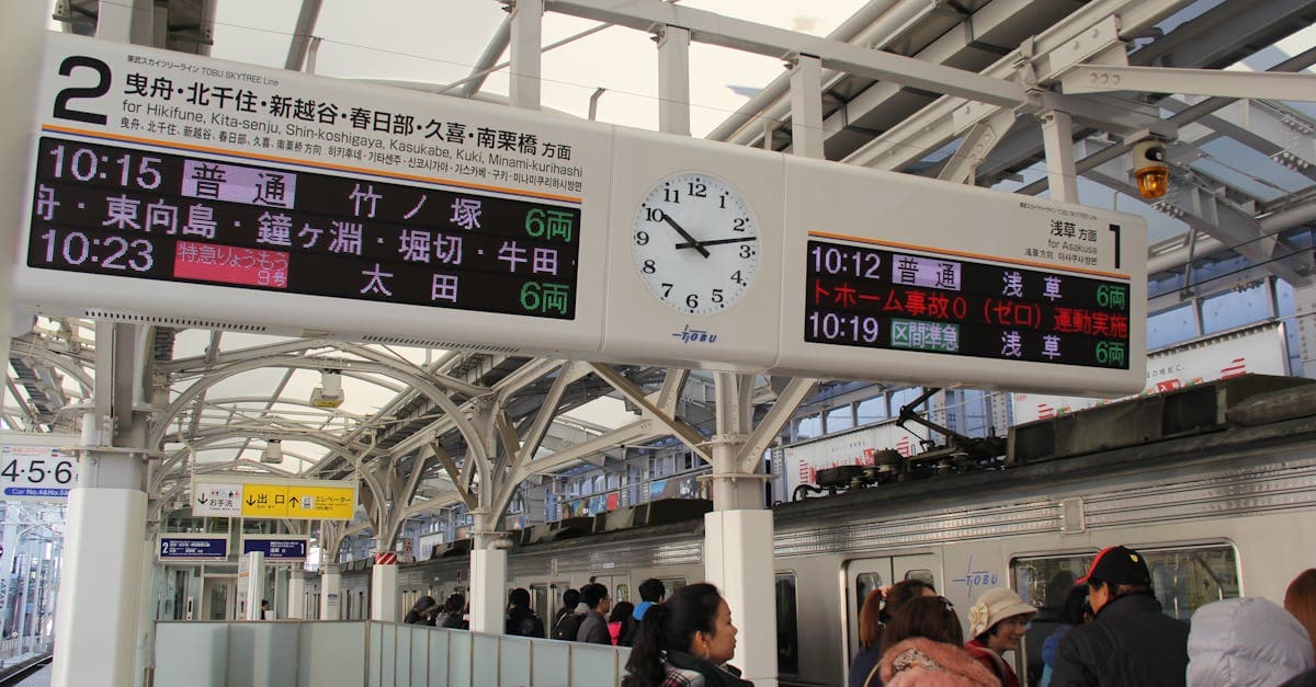 Passageiros aguardando em plataforma de trem japonesa com relógio e painel de horários visíveis