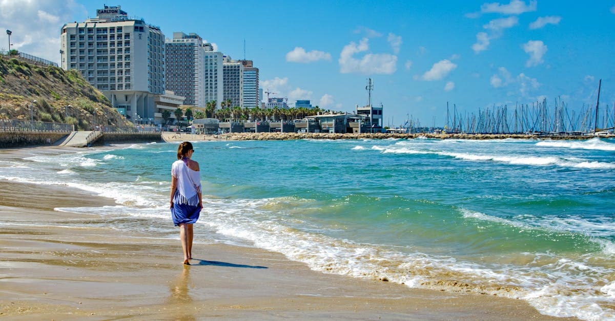 תיירת מטיילת בחוף חולי לאורך הים בעיר מודרנית בימי חופשת פסח 2026