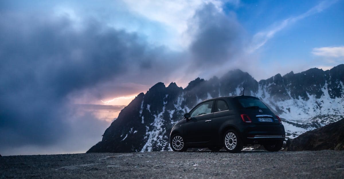 Auto compatta nera ferma su una strada di montagna con vista sulle cime innevate, simbolo del miglior road trip europeo