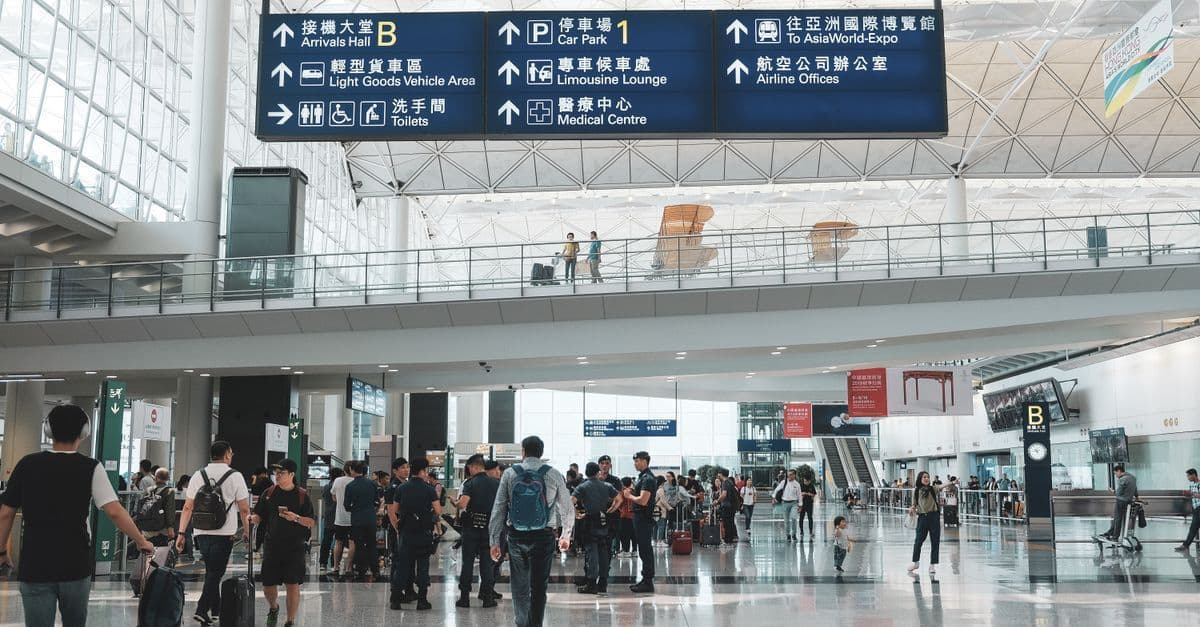 Travelers gather beneath airport signs for arrivals, baggage claim, car parks and transport, with no visa information visible.