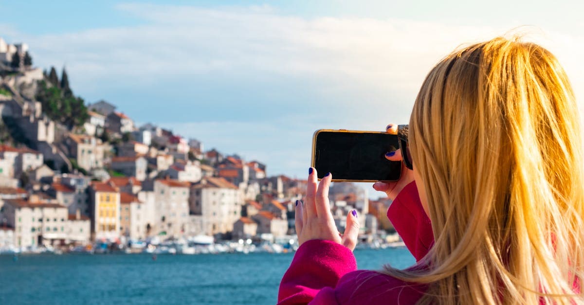 Woman photographing the Šibenik waterfront with her smartphone, staying connected with the best eSIM for Europe 2026.