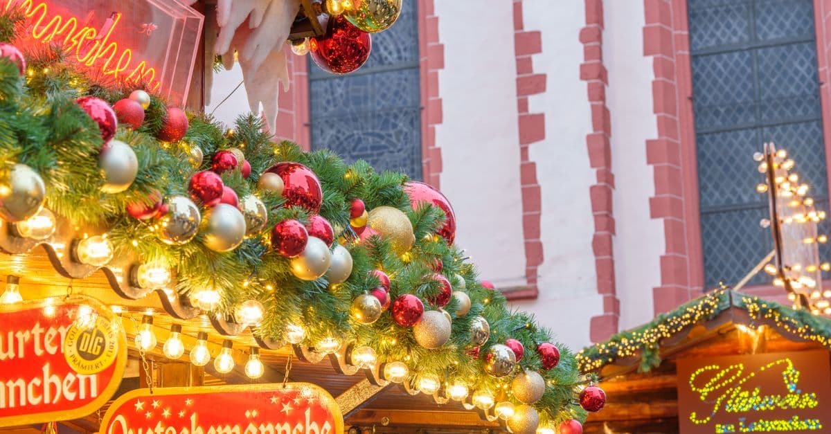 赤や金のオーナメントと電飾で飾られたクリスマスマーケットの屋台が、建物の前に並んでいる。