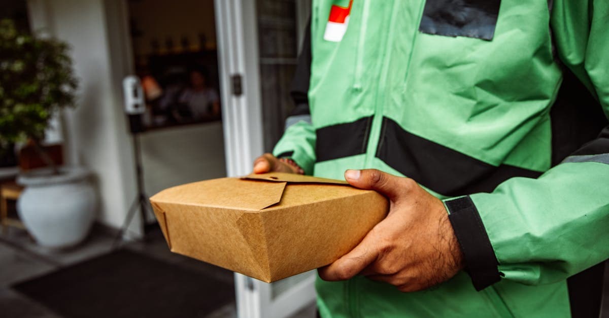 Lieferbote im grünen Jacket trägt umweltfreundliche Verpackung für Food Meal Delivery vor einem Restaurant.