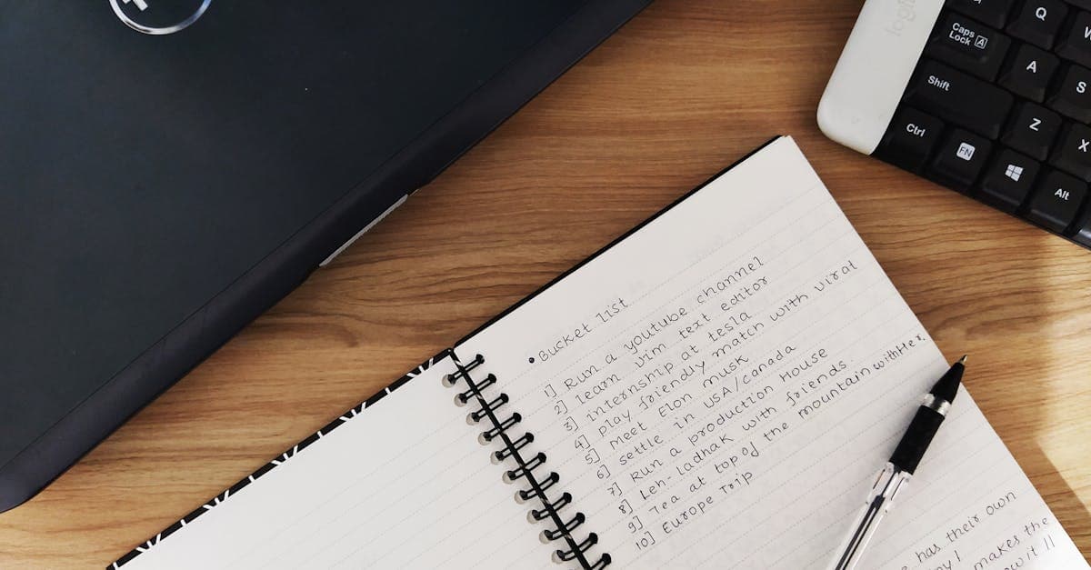 Aufgeschlagenes Notizbuch neben Laptop und Tastatur auf Holzschreibtisch – perfekt zum Planen der eigenen Bucket List.