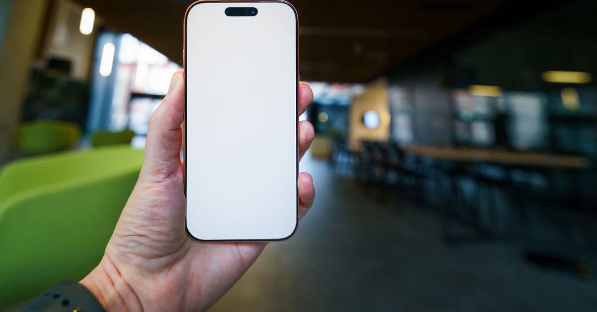 Hand holding a smartphone with blank screen, perfect for mockup purposes inside a modern office environment.