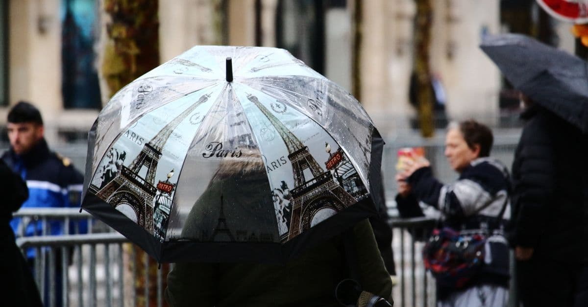 Colorful umbrella with Eiffel Tower print on a rainy Paris street, a common sight during typical paris weather.