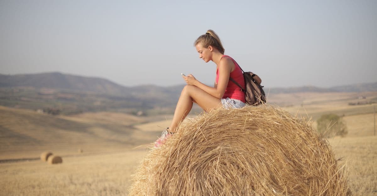 Donna seduta su una balla di fieno in campagna, connessa con una sim solo dati durante il viaggio.
