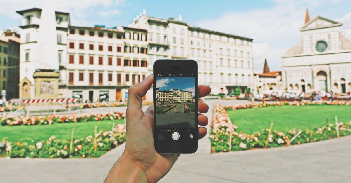 Persona che usa lo smartphone in una piazza storica soleggiata per restare connessa e viaggiare sicuri all'estero.