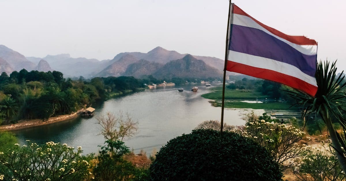 Scenic Kanchanaburi river with a Thai flag in the foreground, answering is thailand safe to visit