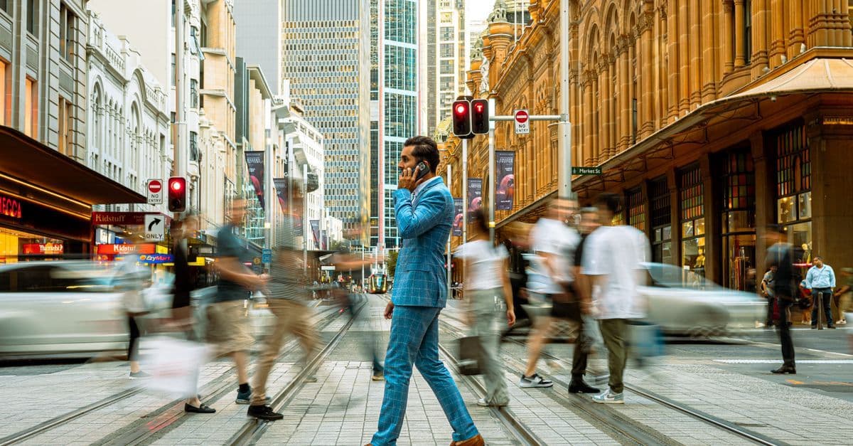 Professionista in abito blu attraversa una strada affollata di Sydney, simbolo degli italiani che lavorano all'estero.