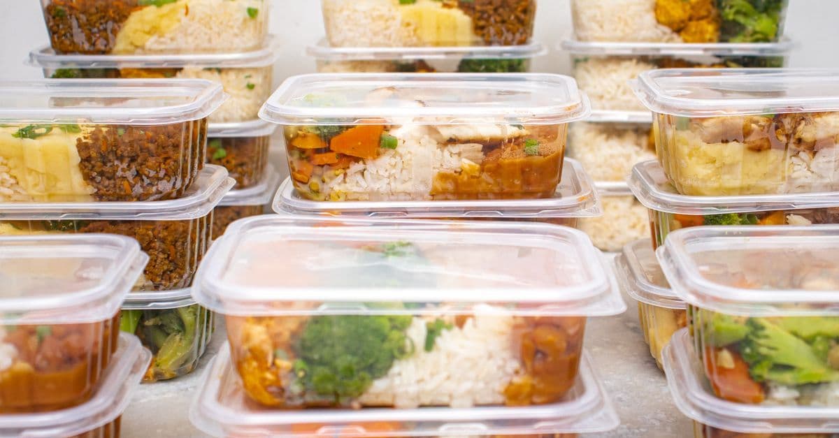 Mehrere Mahlzeit-Behälter mit Reis und Gemüse für proteinreiche Ernährung per Lieferservice.