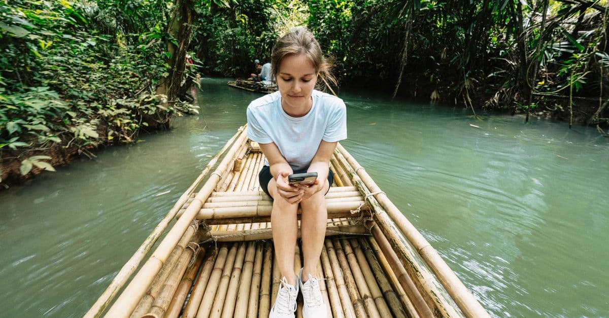 Junge Frau nutzt ihr Smartphone auf einem Bambusfloß im Dschungel von Krabi, Thailand