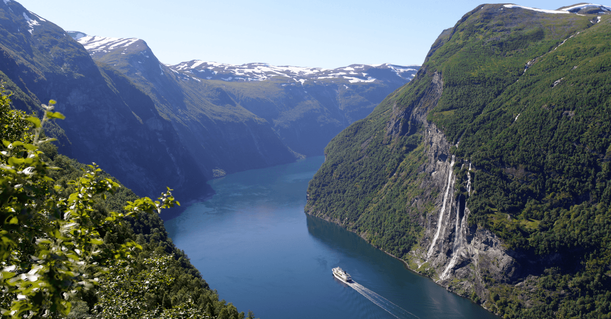 Sun-drenched Geiranger Fjord with lush green mountains and a cruise ship, highlighting summer warmth in Norway