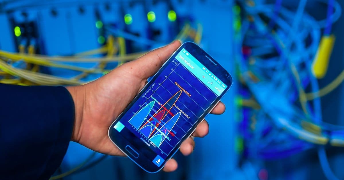 Hand met smartphone die netwerkanalyse toont in een professionele serveromgeving.