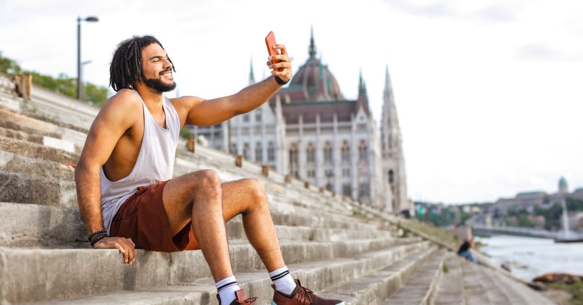 Tourist nutzt sein Smartphone für ein Selfie auf historischen Stufen am Donauufer in Budapest
