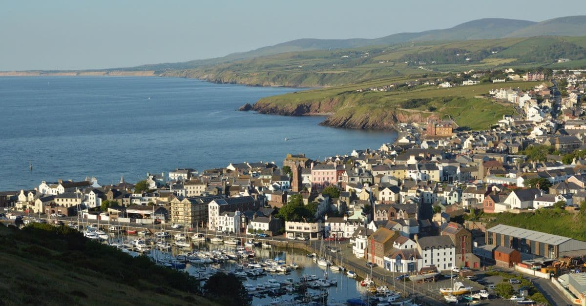 Hamnen i Peel på Isle of Man, med båtar i marinan, hus längs kajen och gröna kullar längs kusten.