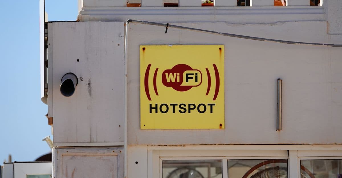 Gul skylt med wifi hotspot på en byggnadsfasad i Cala Rajada, symbol för uppkoppling utomlands.