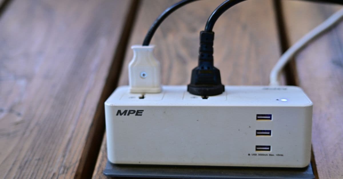 ปลั๊กพ่วงสีขาวเสียบปลั๊กไฟสองช่องและมีพอร์ต USB สามช่อง วางอยู่บนพื้นไม้