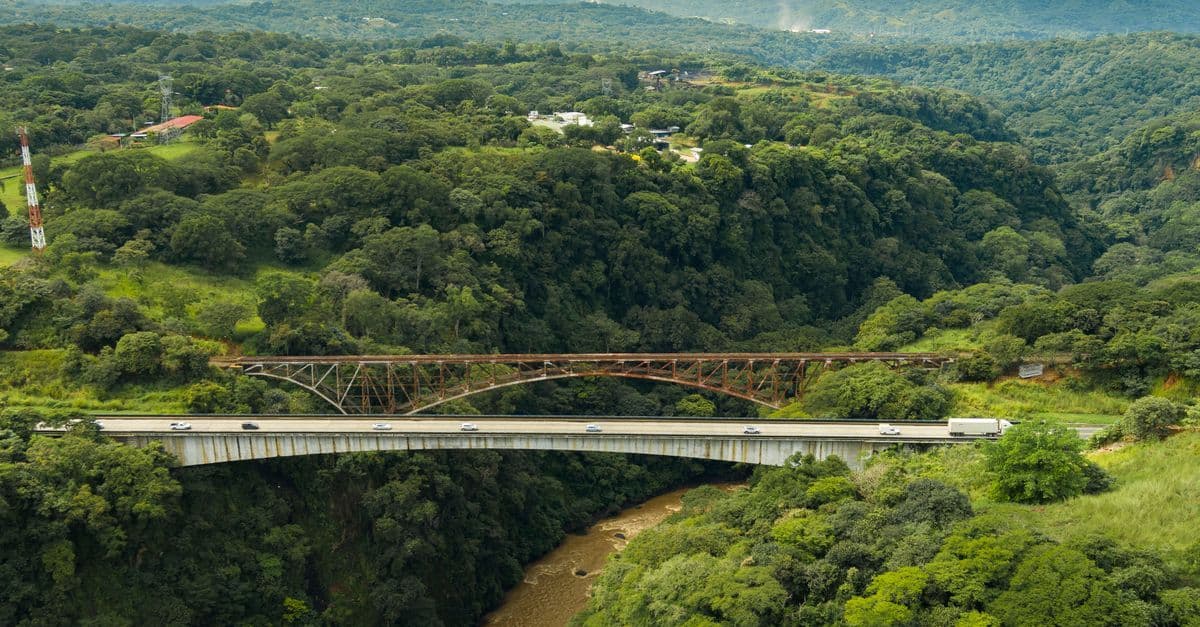 A highway bridge and railway span a forested ravine, with a river winding below.