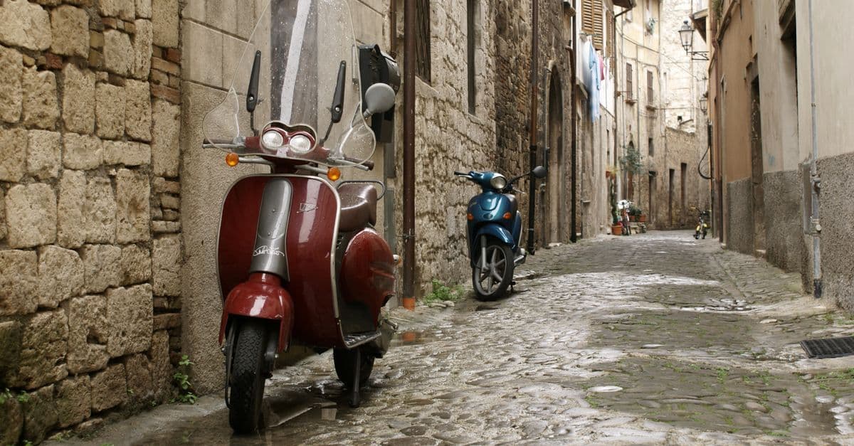 Vicolo acciottolato italiano con scooter d'epoca e architettura in pietra, tipica zona ZTL del centro storico.