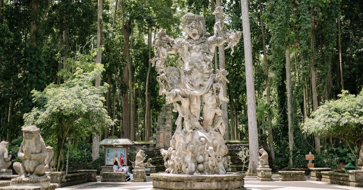 Patung batu berukir detail dikelilingi pepohonan tinggi di taman wisata Ubud yang asri