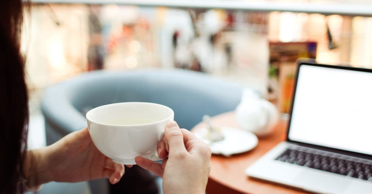 Woman relaxing with a hot drink beside an open laptop in a bright, modern café