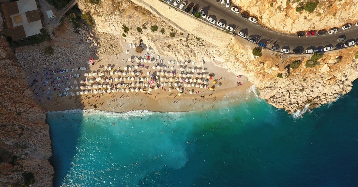 Luftaufnahme des Kaputaş-Strands in der Provinz Antalya mit Sonnenschirmen, türkisblauem Wasser und Küstenstraße am Fels.