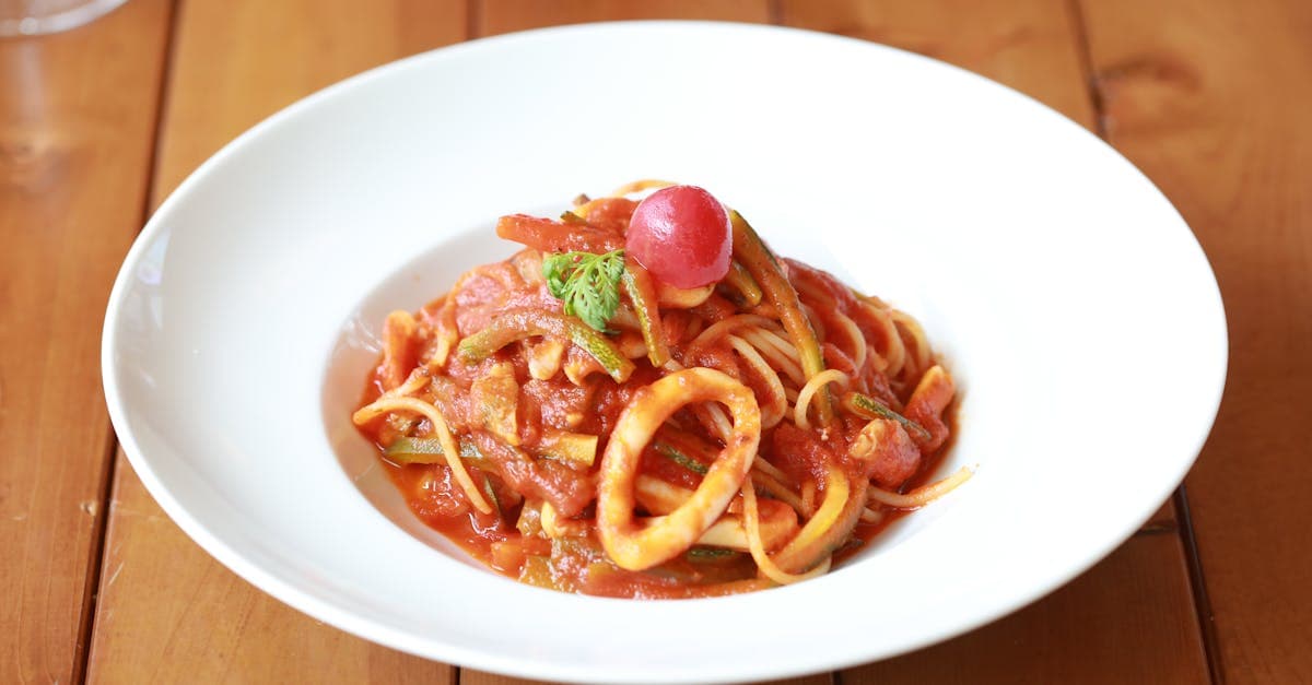 A plate of spaghetti served with a flavorful tomato sauce and garnish on a wooden table.