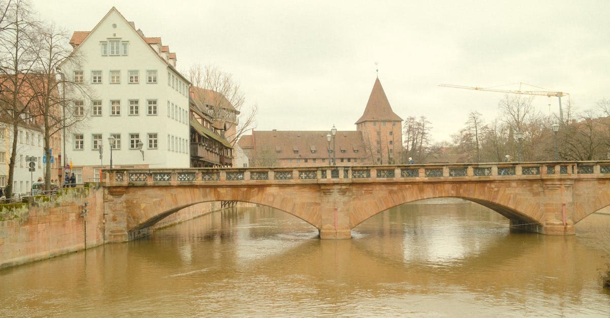 Scenic view of a historic bridge in Nuremberg over a calm river with cloudy skies.