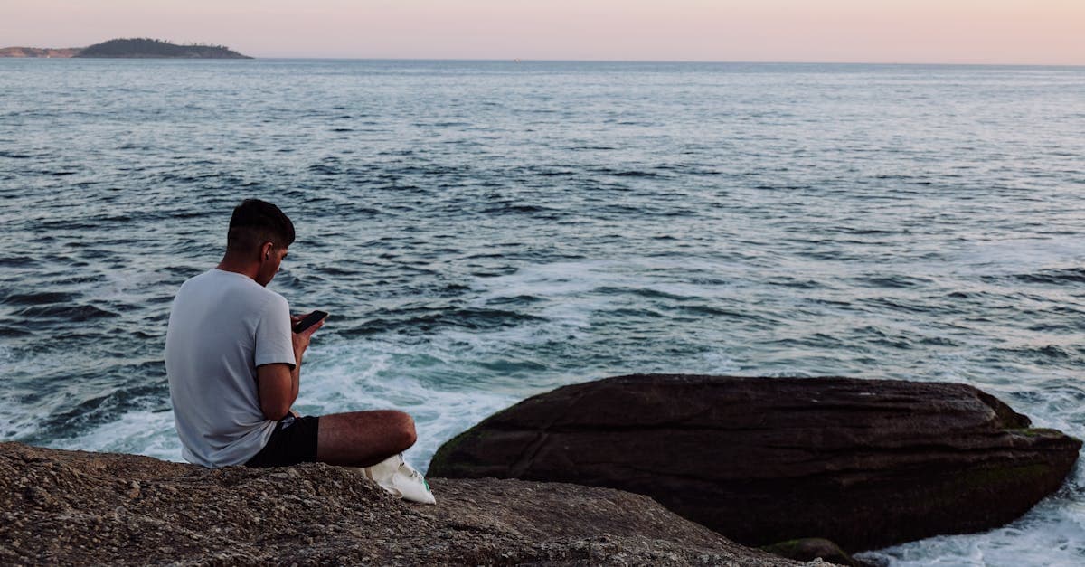 Homem usando smartphone à beira-mar no Rio de Janeiro ao pôr do sol, conectado via roaming de dados