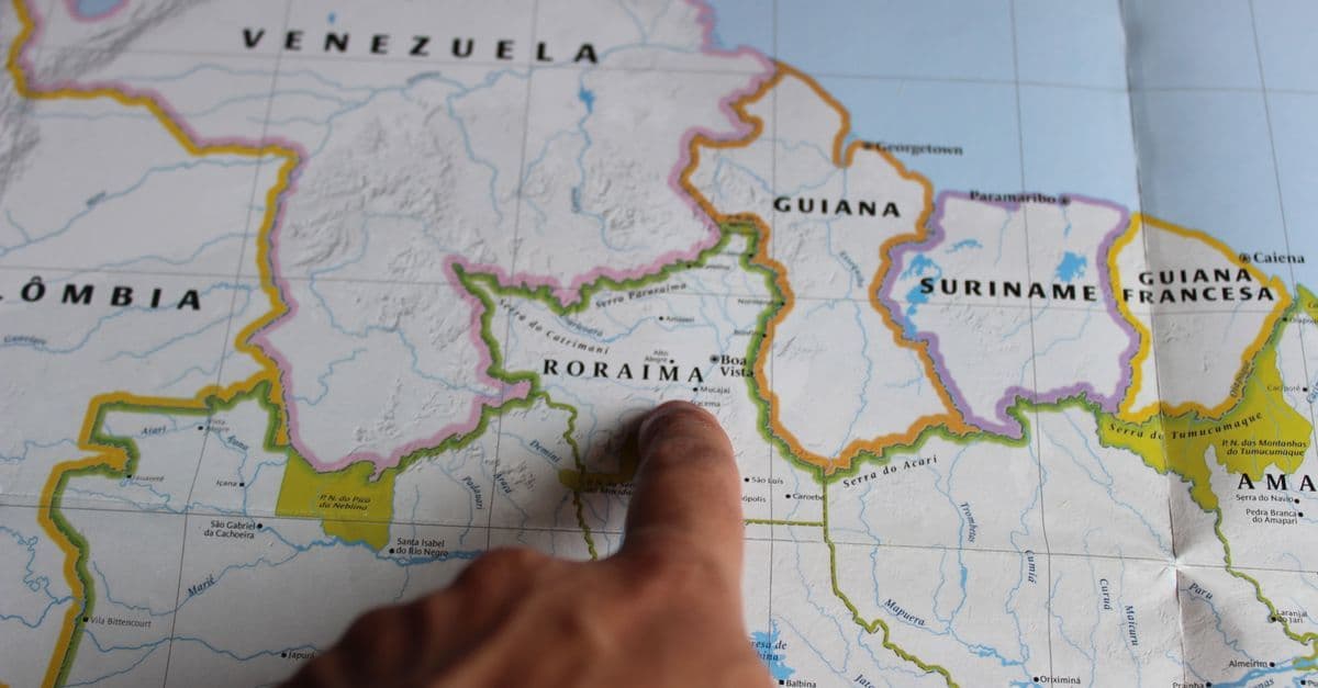 Dedo indicando região em mapa detalhado, representando a localização geográfica de territórios ultramarinos ao redor do mundo.
