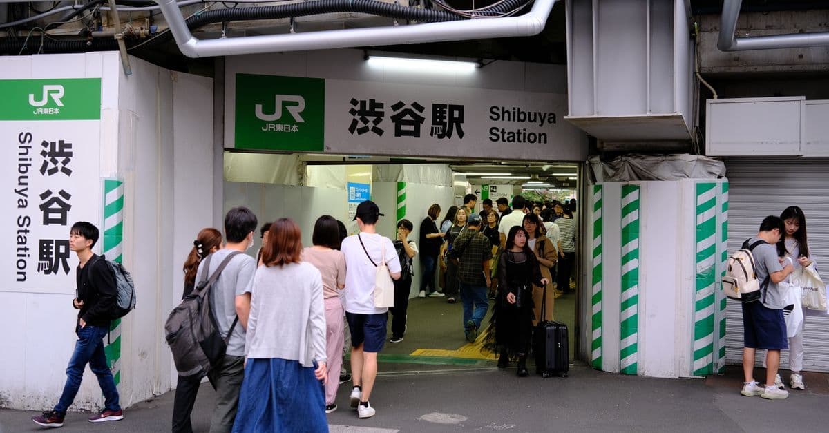 Commuters pass through the entrance to Shibuya Station, with bilingual signs above the doorway.