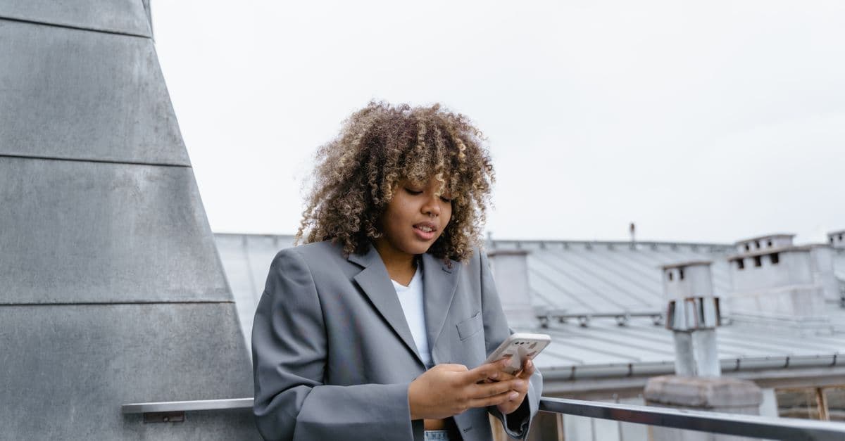 Jovem mulher de cabelo cacheado usando smartphone em terraço, curiosa sobre o que é esim