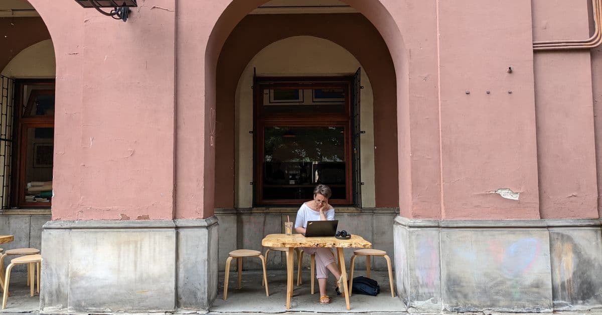 Kobieta pracująca na laptopie przed kawiarnią w Warszawie, idealna ilustracja stylu work and travel.