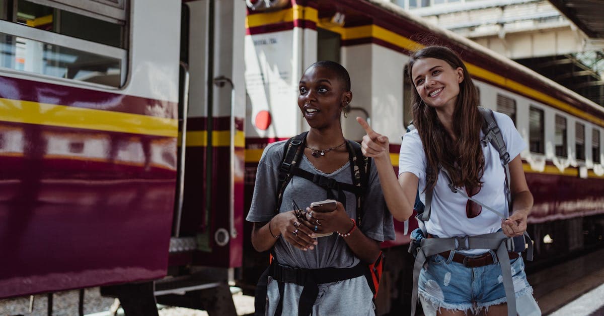 Two women with backpacks laughing at a Southeast Asian city train station, ready for their adventure