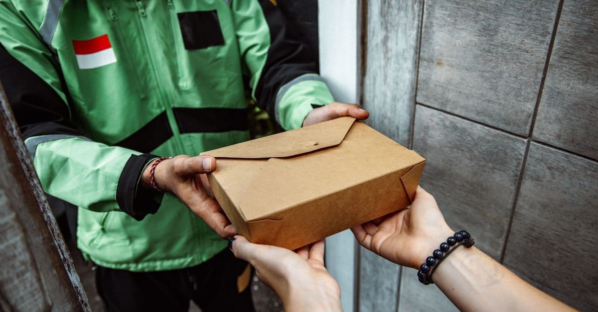 Zusteller übergibt Lunchbox an Kunden – moderner food meal delivery Service im Alltag.