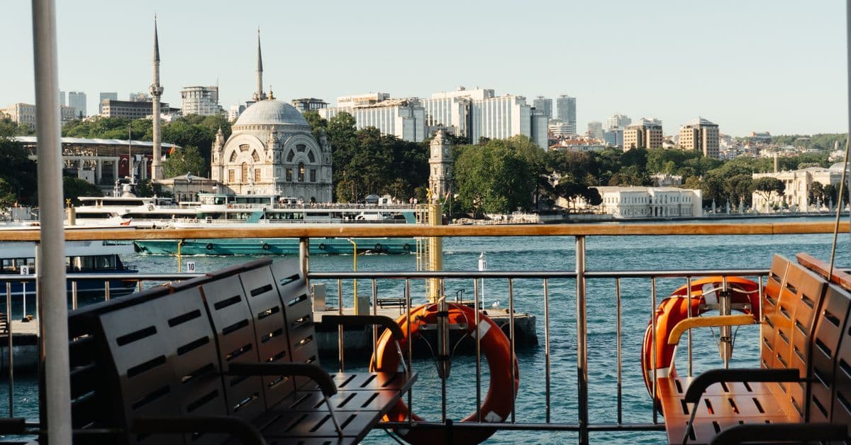 Blick vom Deck einer Fähre mit Sitzbänken und Rettungsringen auf eine Moschee am Istanbuler Ufer.