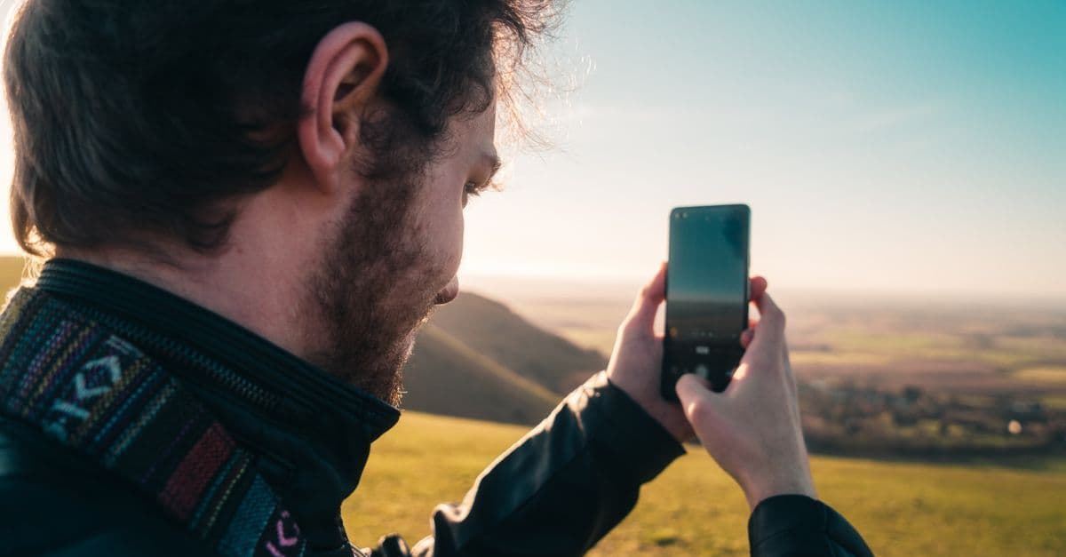 Man using a smartphone to capture a sunny coastal scene in Brighton, England.